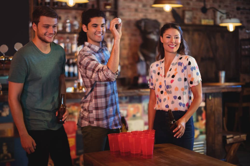 Drei Freunde spielen gemeinsam Beerpong und sind gut gelaunt